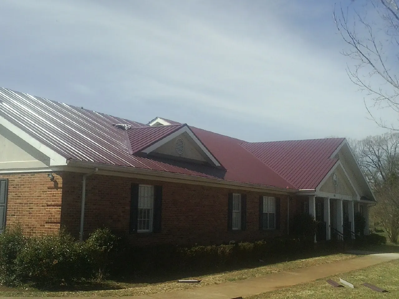 Red metal roof with gabled entries on a long brick building, from a Hail Damage Roof Repair job in Buckholts