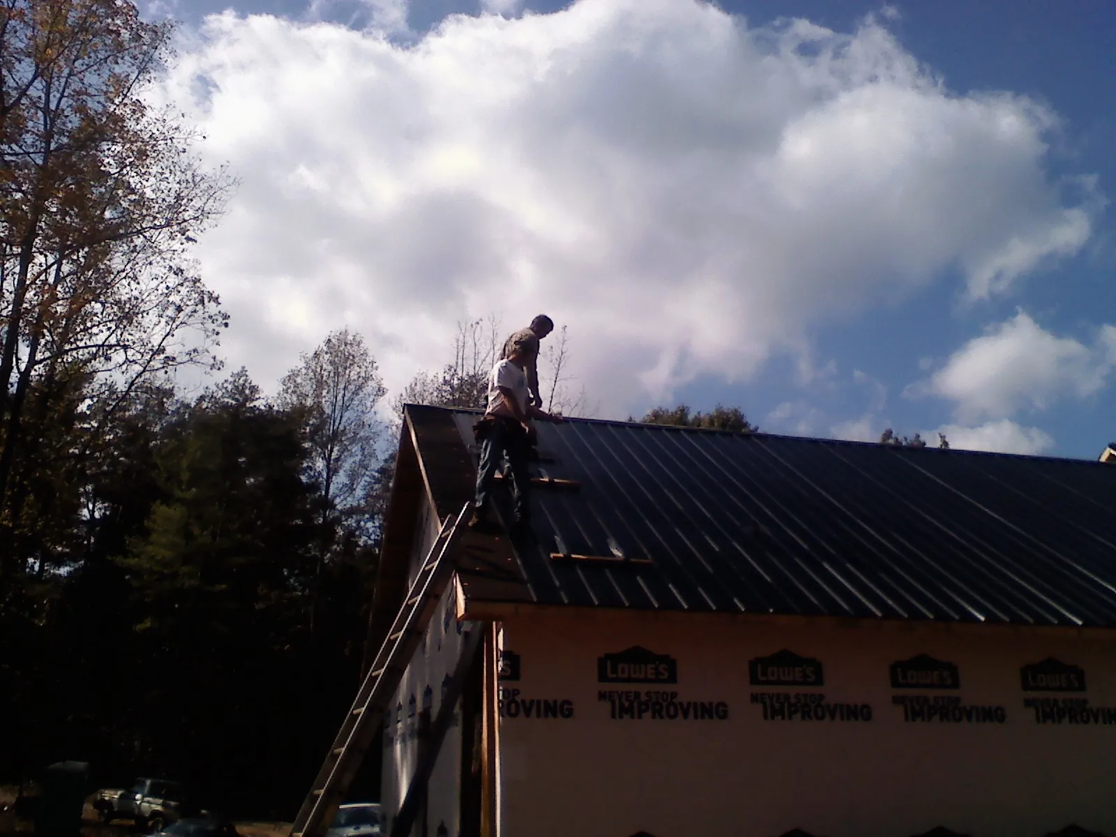 Roofer fastening dark metal panels high against a cloudy sky, from a Roof Inspection job in Buckholts