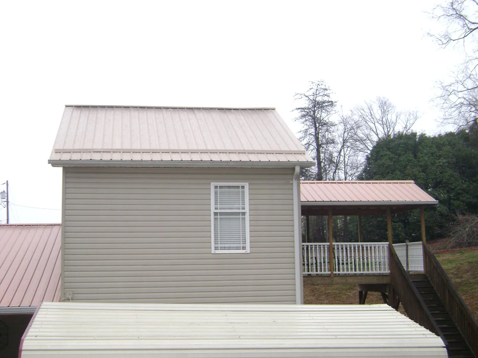 Tan metal roofs on a two story addition and attached porch, from a Roof Replacement job in Buckholts